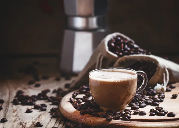 Kaffee mit Milch in einer Glastasse, Kaffeebohnen in Leinensäcken — Stockfoto