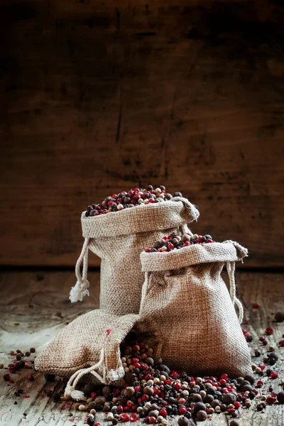 Svart, rosa, vitpeppar och kryddpeppar i säckväv säckar — Stockfoto