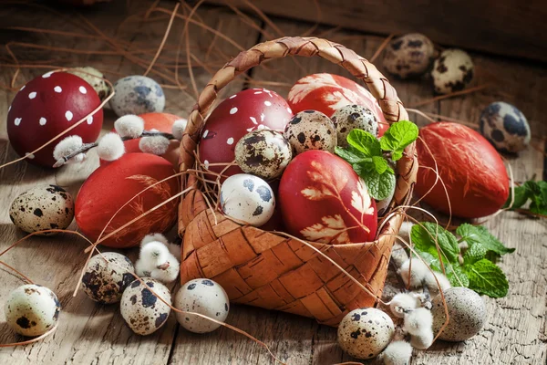 Painted eggs and speckled quail eggs in a wicker basket — Stock Photo, Image