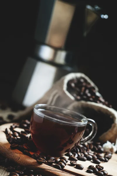 Café negro en una taza sobre un fondo de bolsas de café con una cafetera — Foto de Stock