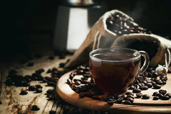 Schwarzer Kaffee in einer Tasse auf einem Hintergrund aus Kaffeesäcken mit einer Kaffeemaschine — Stockfoto