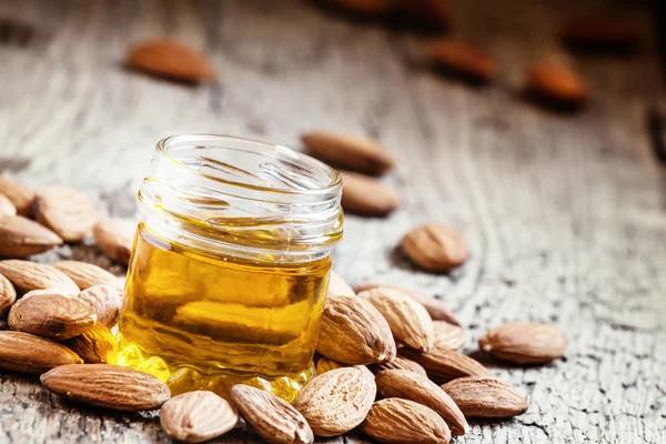 Huile d'amande dans un petit bocal d'amandes et de noix sur un vieux fond de bois — Photo