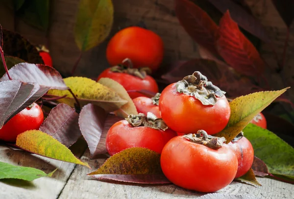 Persimmons with leaves on the old wooden table — Stock Photo, Image