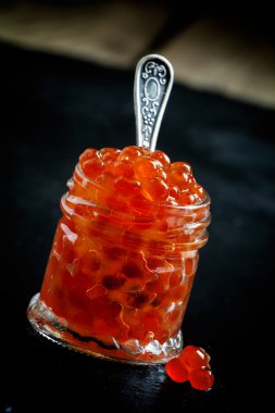 Siyah taş zemin üzerine cam kavanozda kırmızı havyar 