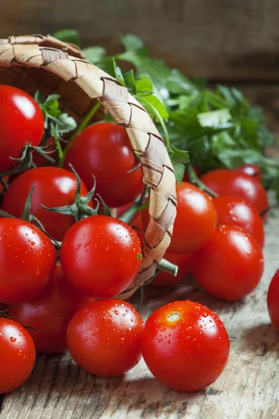 Små röda körsbärstomater läcker ut en flätad korg — Stockfoto