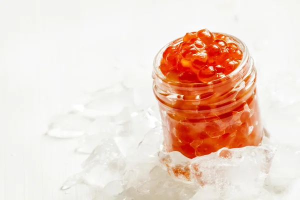 Red salmon caviar in a glass jar on crushed ice — Stock Photo, Image