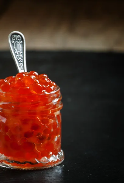 Red caviar in a glass jar on black stone background