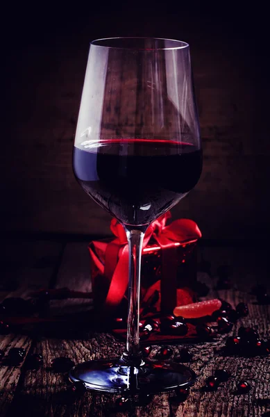Vino rosso in un bicchiere, un regalo nell'imballaggio rosso — Foto Stock