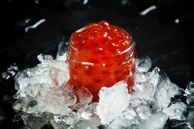 Delicious red caviar in a glass jar on crushed ice 