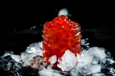 Delicious red caviar in a glass jar on crushed ice 