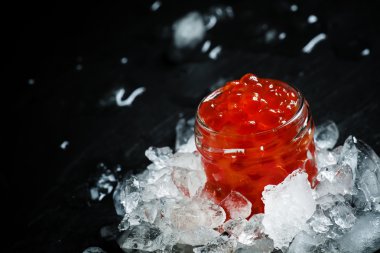 Delicious red caviar in a glass jar on crushed ice 