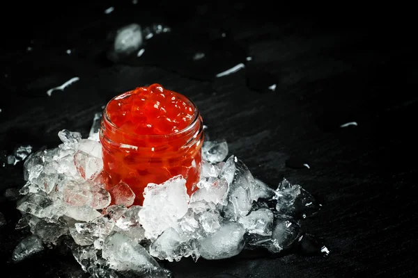 Delicioso caviar vermelho em um frasco de vidro em gelo picado — Fotografia de Stock