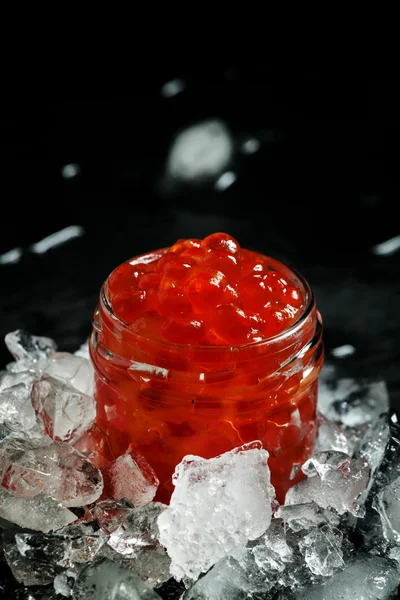 Delicioso caviar rojo en un frasco de vidrio sobre hielo picado — Foto de Stock