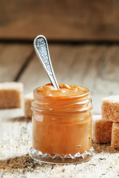 Dulce caramelo líquido en un frasco pequeño y azúcar de caña morena — Foto de Stock