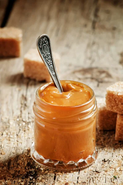 Sweet liquid caramel in a small jar and brown cane sugar — Stock Photo, Image
