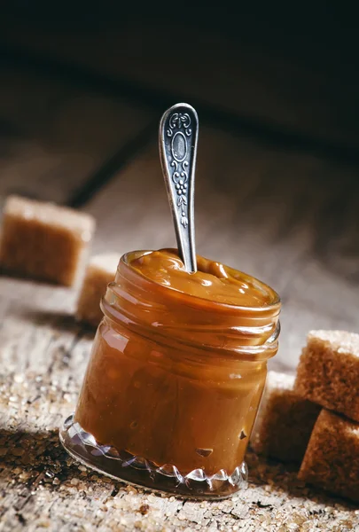 Sweet liquid caramel in a small jar and brown cane sugar — Stock Photo, Image