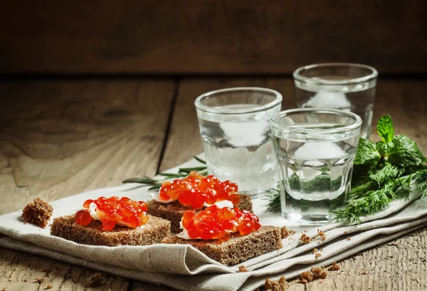 Vodka russa fria com gelo e pequenos lanches sanduíches com caviar — Fotografia de Stock