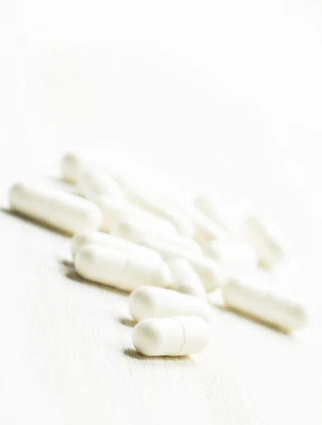 Таблетки в капсулах на білому дерев'яному фоні — стокове фото