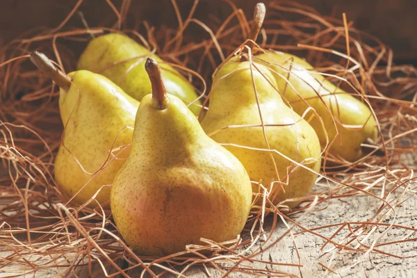 Gelbe Birnen im trockenen Stroh auf dem Holztisch — Stockfoto