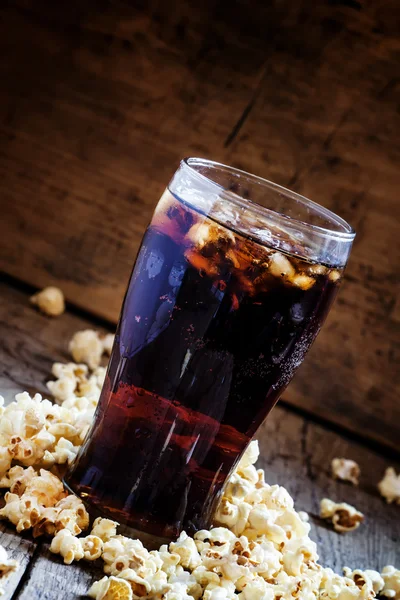 Grande bicchiere di cola, popcorn salati versati sul tavolo — Foto Stock