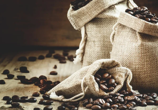 Grani di caffè torrefatto in sacchetti su vecchio tavolo di legno — Foto Stock