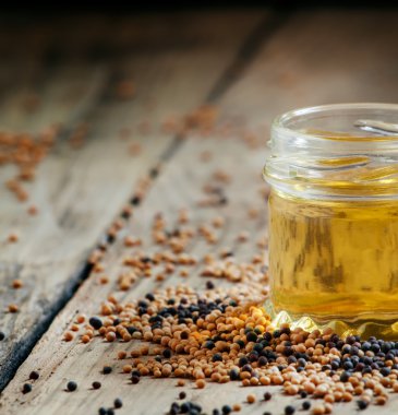 Oil of mustard in a small jar and yellow and black mustard seeds 
