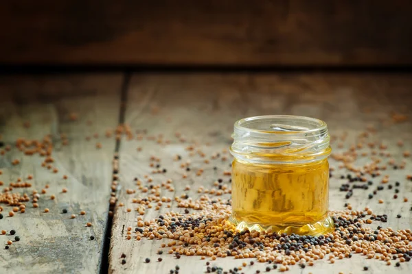 Aceite de mostaza en un frasco pequeño y semillas de mostaza amarillas y negras —  Fotos de Stock