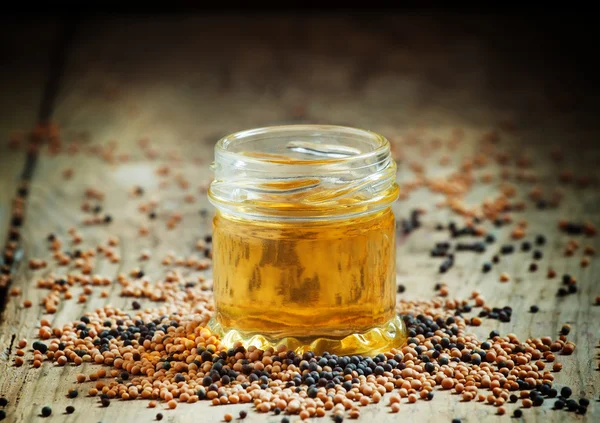 Oil of mustard in a small jar and yellow and black mustard seeds — Stok fotoğraf