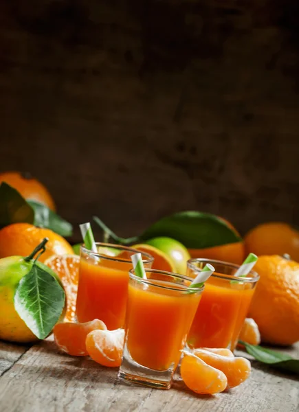 Свежий сок спелых мандаринов в маленьком стакане с полосатыми соломинками — стоковое фото