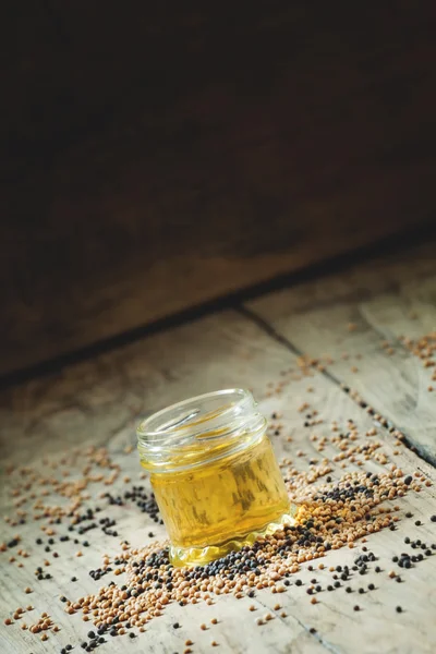 Oil of mustard in a small jar and yellow and black mustard seeds — Stok fotoğraf