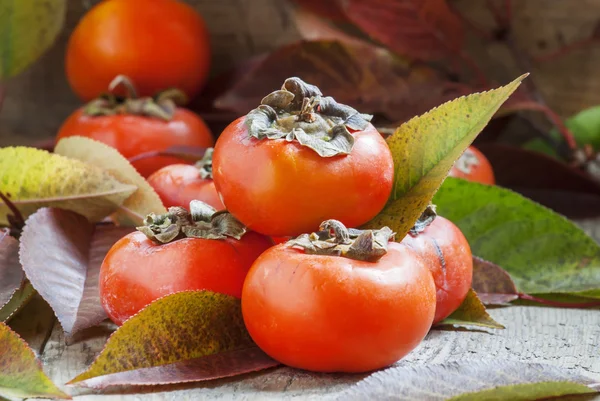 Persimmons with leaves on the old wooden table — Stock Photo, Image