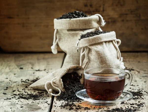 Стеклянная прозрачная чашка черного чая и сухой чай в мешках — стоковое фото