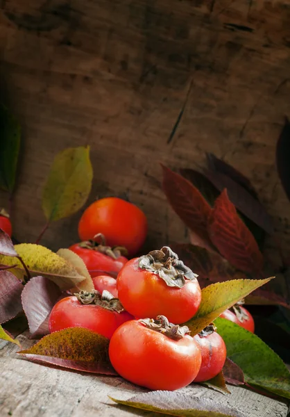 Persimmons with leaves on the old wooden table — Stock Photo, Image