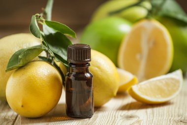 Essential oil of lemon and fresh lemons on the old wooden background clipart