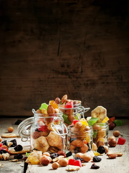 Nuts and dried fruits in glass jars on the old wooden table — Stock Photo, Image