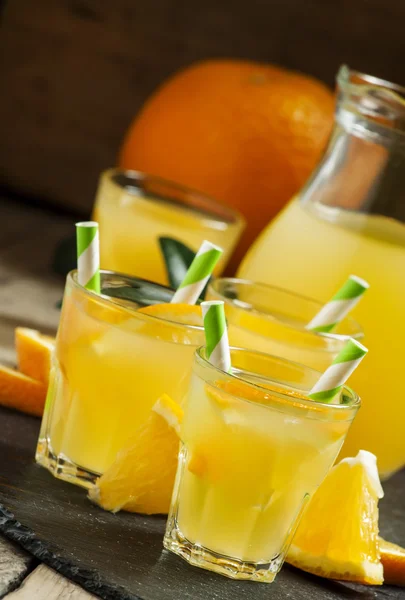 Апельсиновый напиток в маленьких стаканах с полосатыми соломинками и кувшином — стоковое фото