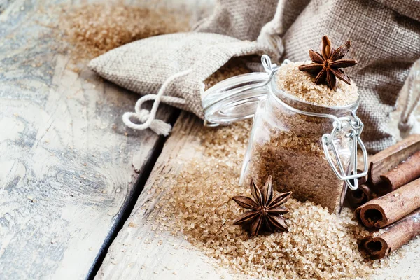 Açúcar de cana marrom em sacos feitos de serapilheira e um frasco de vidro com um anis estrelado — Fotografia de Stock