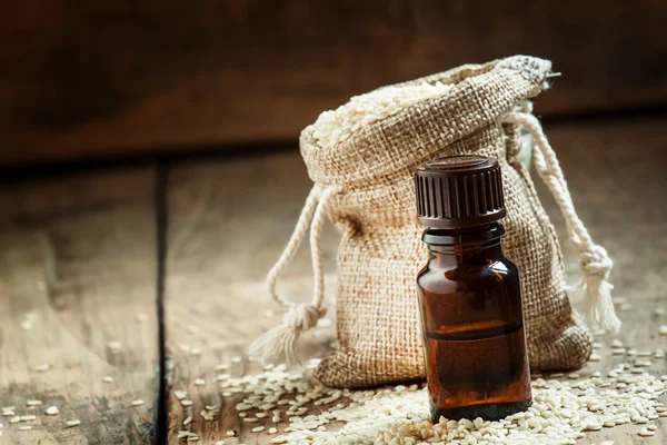 Huile essentielle de sésame dans une bouteille de verre brun et graines de sésame — Photo