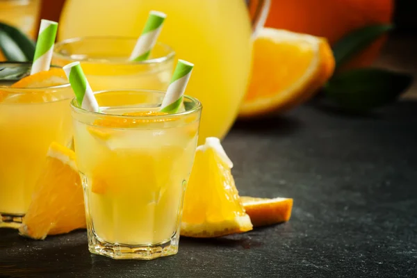 Orange drink in small glasses with striped straws and pitcher