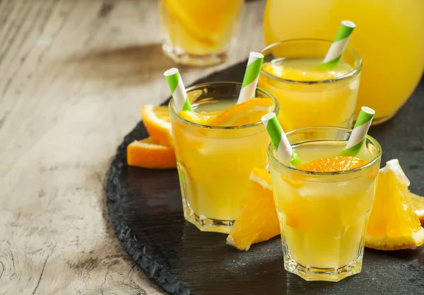 Bebida laranja em copos pequenos com palhas listradas e jarro — Fotografia de Stock