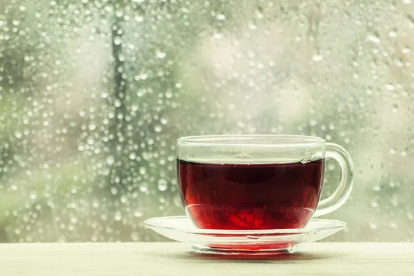 Xícara de chá preto quente no fundo borrado da janela molhada — Fotografia de Stock