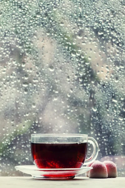 Taza de té negro caliente sobre el fondo borroso de la ventana húmeda — Foto de Stock