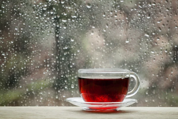 Cup of hot black tea on the blurred background of wet window — Stock Photo, Image