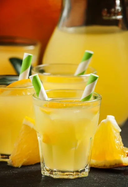 Boisson orange en petits verres avec pailles rayées et pichet — Photo