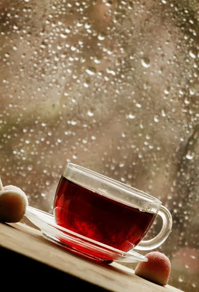 Taza de té negro caliente sobre el fondo borroso de la ventana húmeda — Foto de Stock