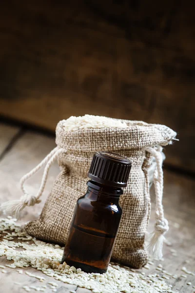 Aceite esencial de sésamo en una botella de vidrio marrón y semillas de sésamo —  Fotos de Stock