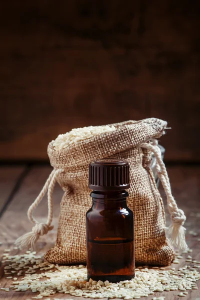 Olio essenziale di sesamo in una bottiglia di vetro marrone e semi di sesamo — Foto Stock