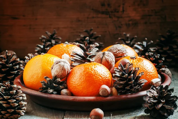 Clay plate with orange mandarins, fir cones, walnuts, hazelnuts and pistachios — Zdjęcie stockowe