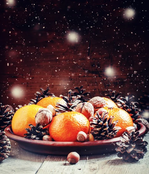 Clay plate with orange mandarins, fir cones, walnuts, hazelnuts and pistachios — Stok fotoğraf