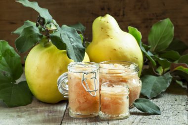 Pink quince jam in glass jars and fresh quince fruits with leaves 